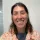 IDP IELTS test taker Sandra indoors - A person with a blurred face wearing a floral-patterned shirt over a dark top, standing indoors near a white wall and a glass window or door
