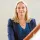 Portrait of Maddalaine Ansell, Director of Education at the British Council. She has blonde hair, is wearing a navy blazer over a blue patterned top, and is standing indoors near a railing